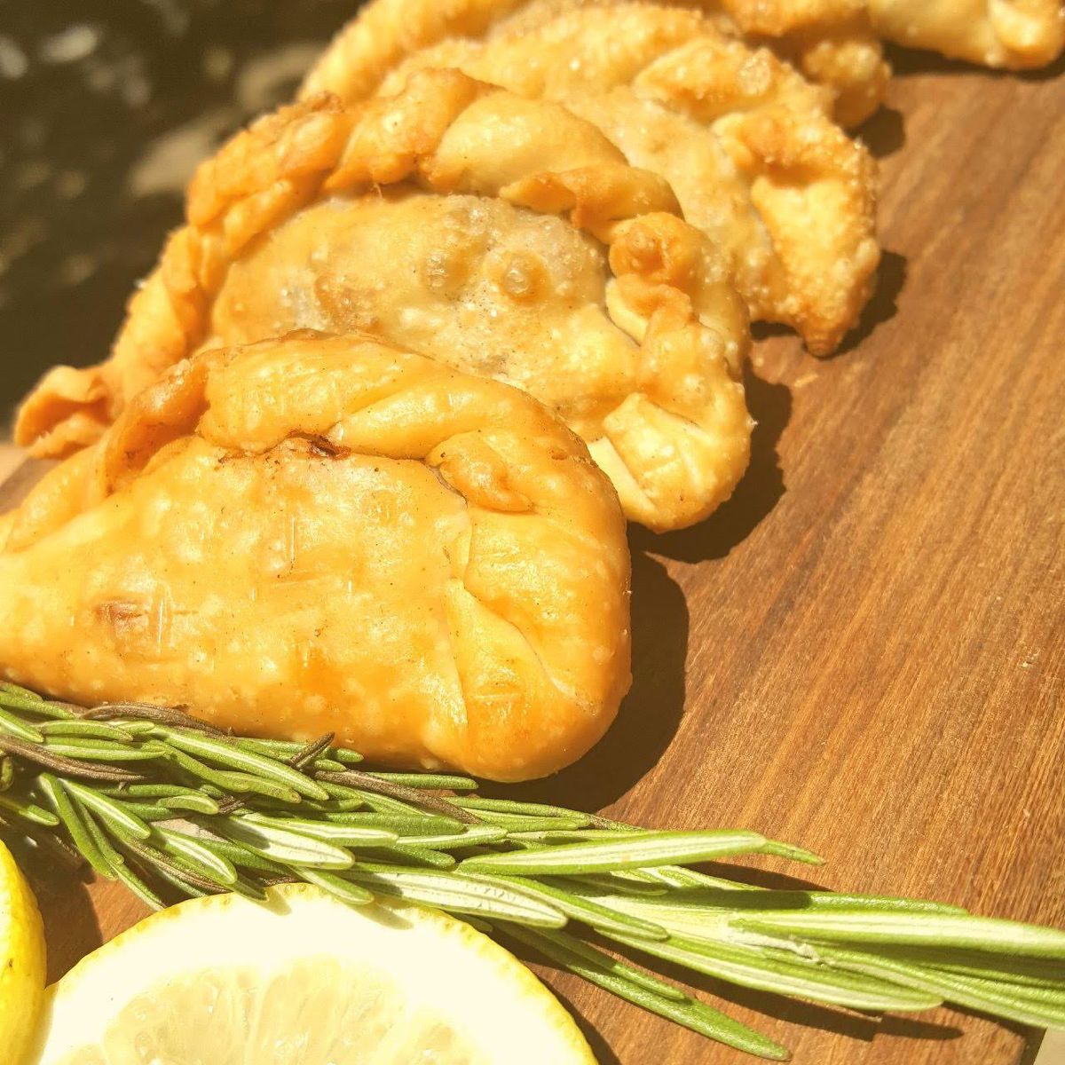 Empanadas criollas fritas sobre tabla con romero